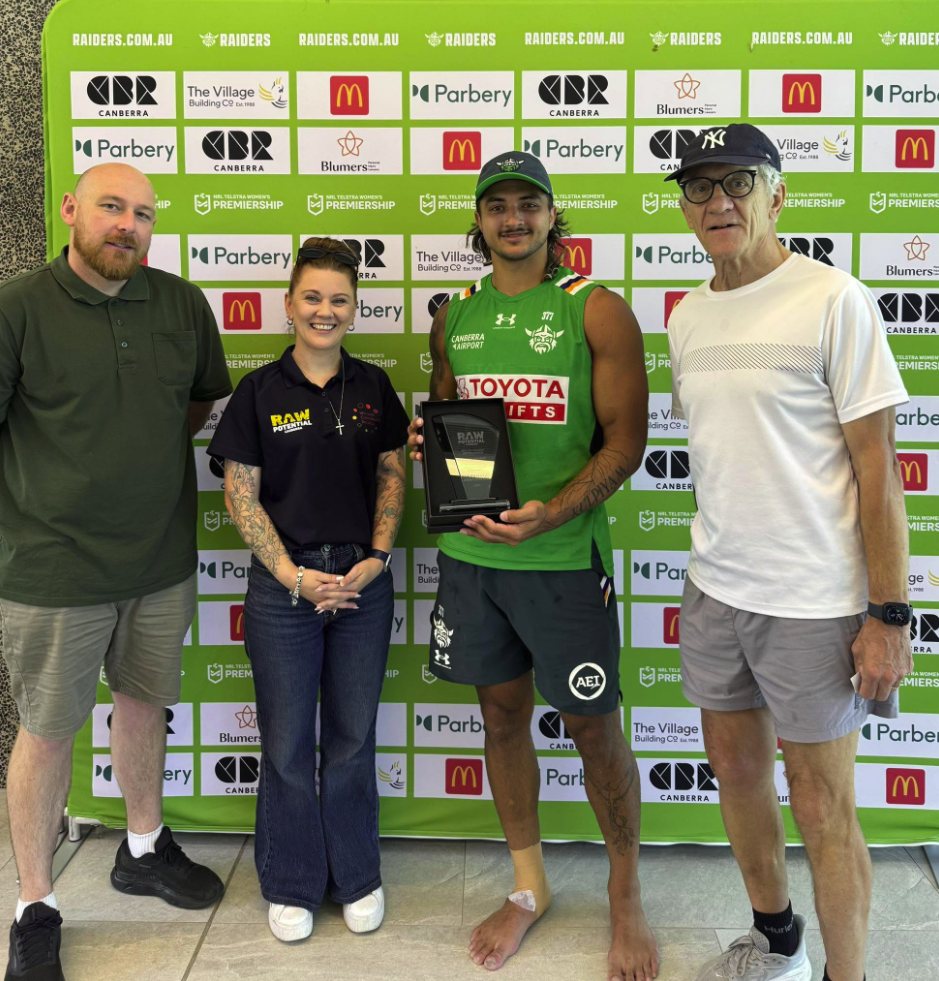 Canberra Raiders player Xavier Savage holding a Raw Potential award, standing with Raw Potential supporters in front of a Raiders media wall
